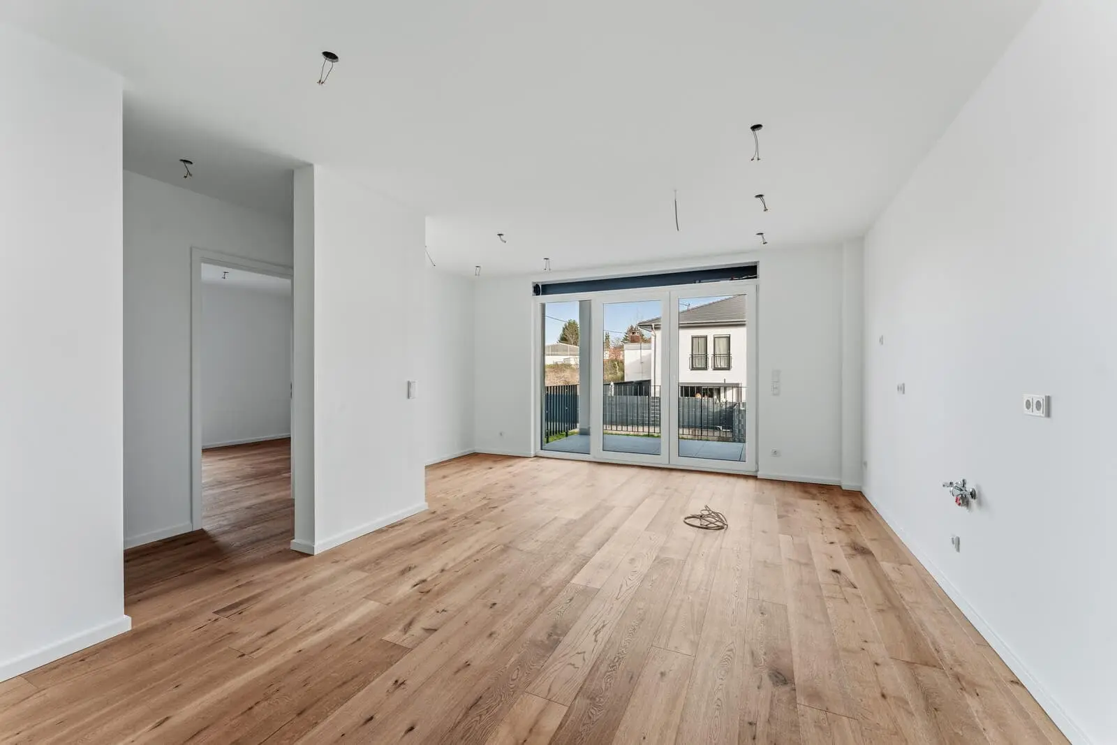 Unfurnished room with white walls, wooden floor, large glass doors leading to a balcony, and exposed ceiling light fixtures.