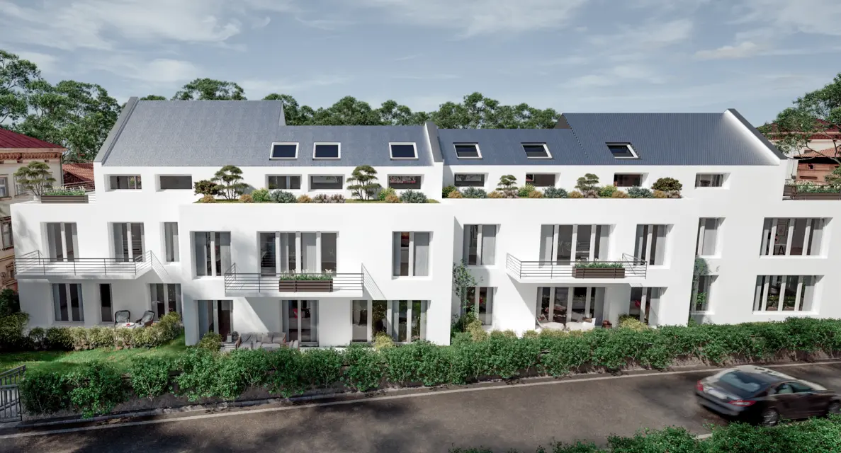 A modern white apartment building with balconies and rooftop gardens, surrounded by greenery, facing a street with parked and passing cars.
