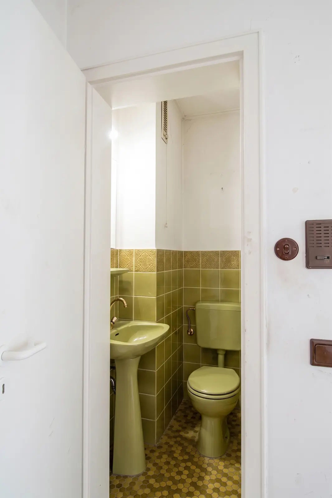A small bathroom with eco-friendly sanitary fittings, including a toilet and a washbasin, and green-tiled walls and floor.