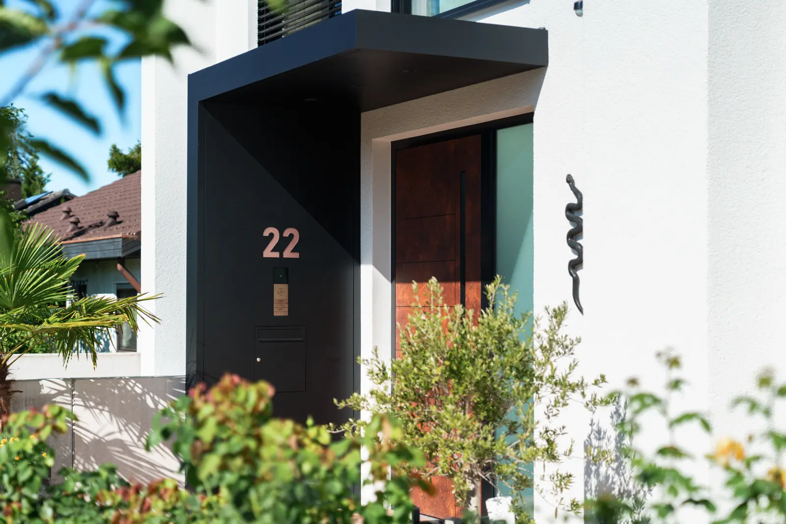 Front door of a white house with the number 22, a wooden door, and a black metal snake wall ornament.