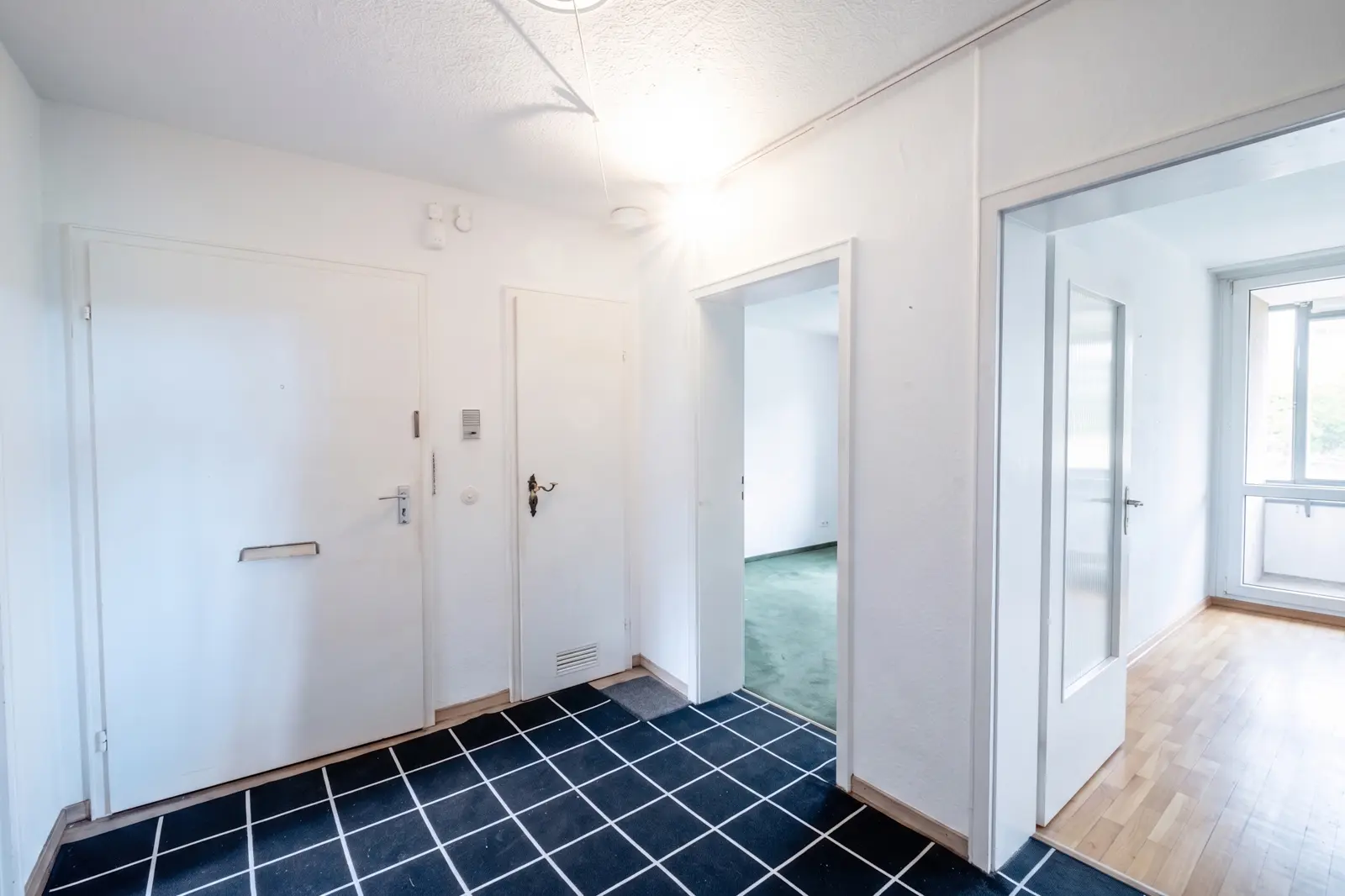 Bright hallway with a tiled floor, white walls, three doors leading to other rooms and daylight coming in from the adjoining rooms.