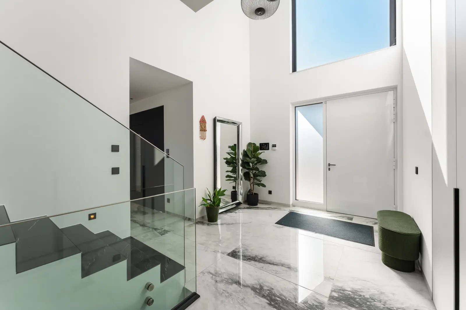 Modern entryway with marble flooring, a glass-railed staircase, a floor-length mirror, a large potted plant, and a white front door.