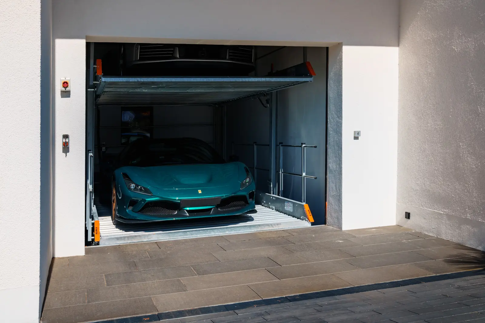 A turquoise Ferrari parked on a mechanical car elevator lift inside a garage.